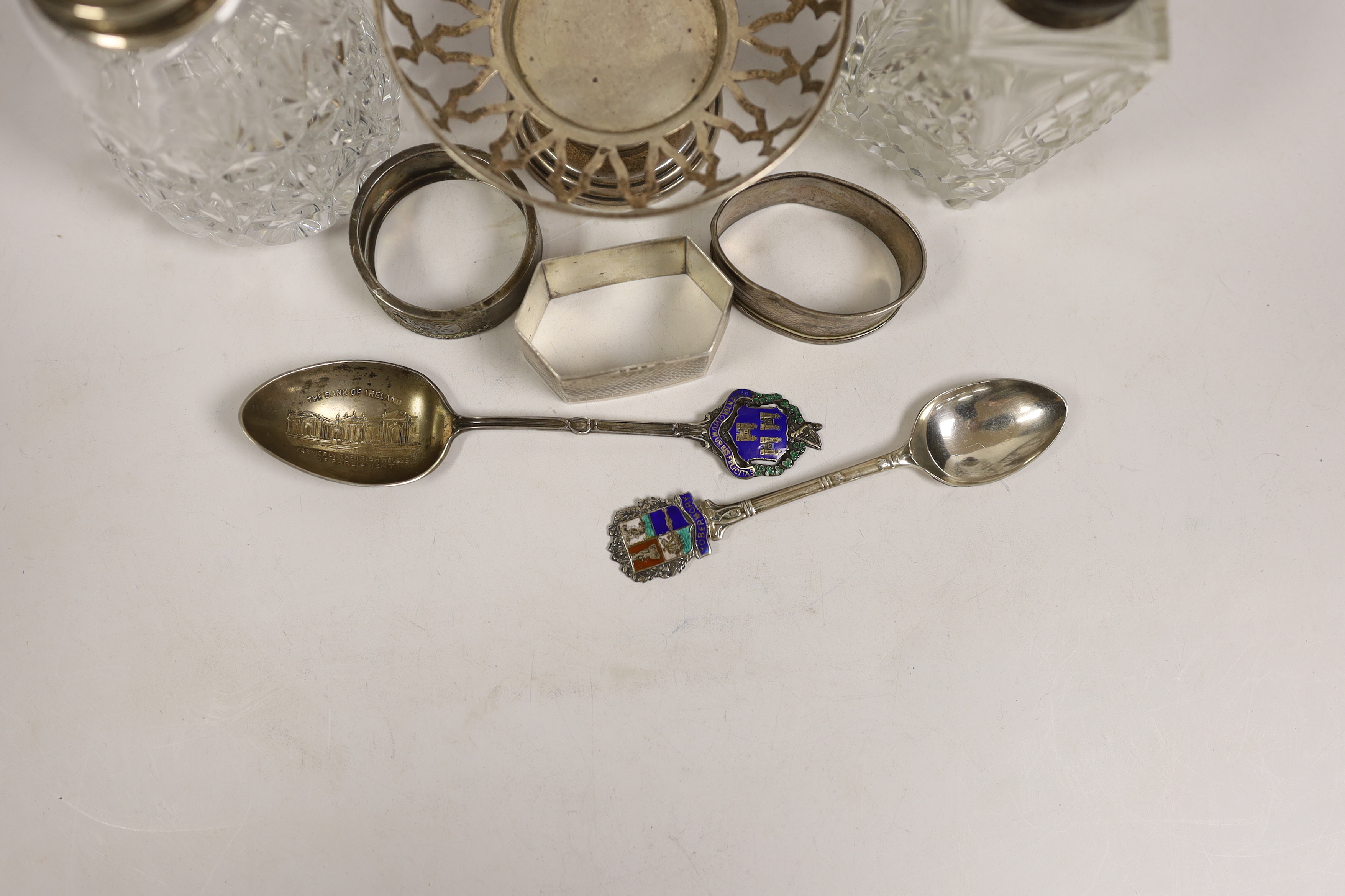 A group of small silver including two mounted glass sugar sifters, three assorted napkin rings, two commemorative spoons and a small pedestal nut dish (lacking insert).